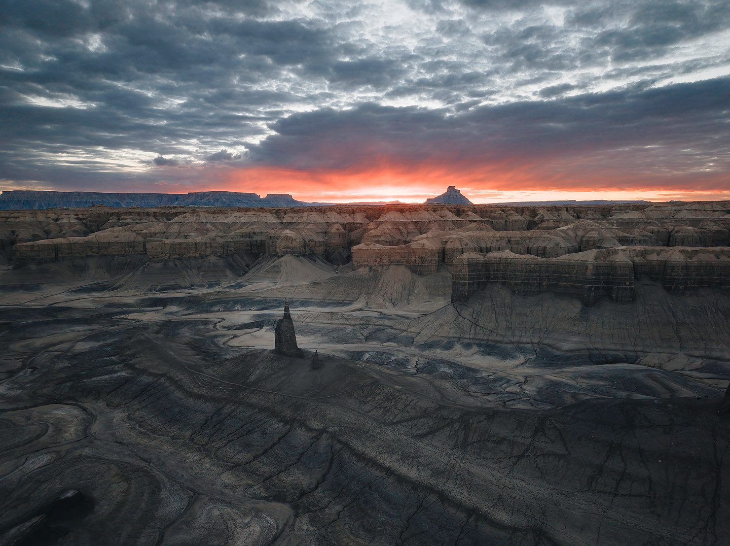 Fiery sunset breaking over dark badlands and a lone rock spire — licensable editorial frame