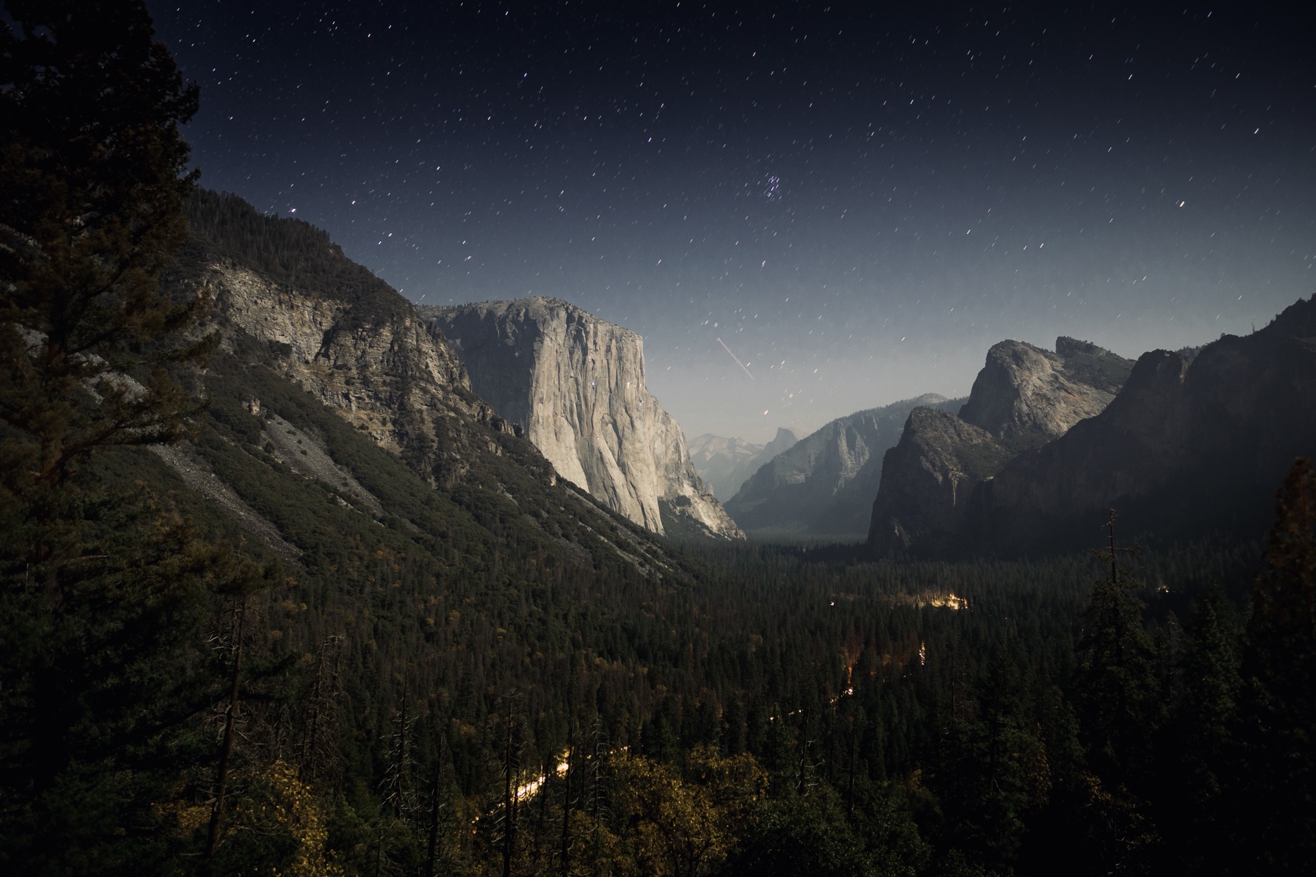 El Capitan beneath a starry sky, faint lights in the valley below.